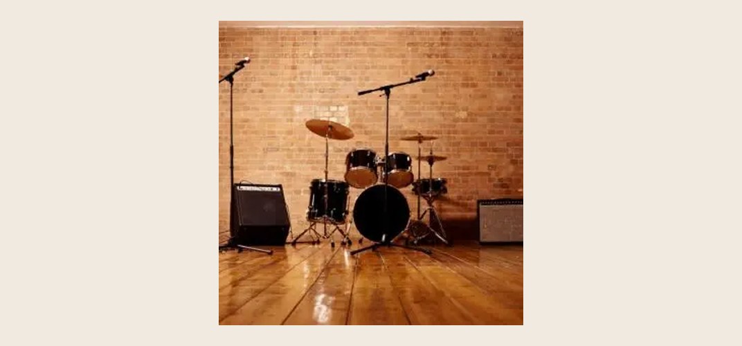 Drum kit and amplifiers set up on a wooden stage against a brick wall