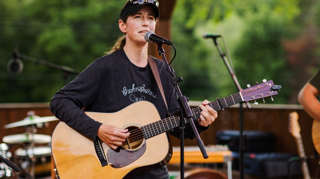 Singer-songwriter Carrie Hinkley playing acoustic guitar outdoors