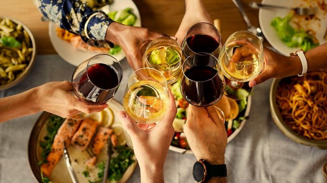 Overhead view of hands raising glasses of red and white wine over a table of shared dishes