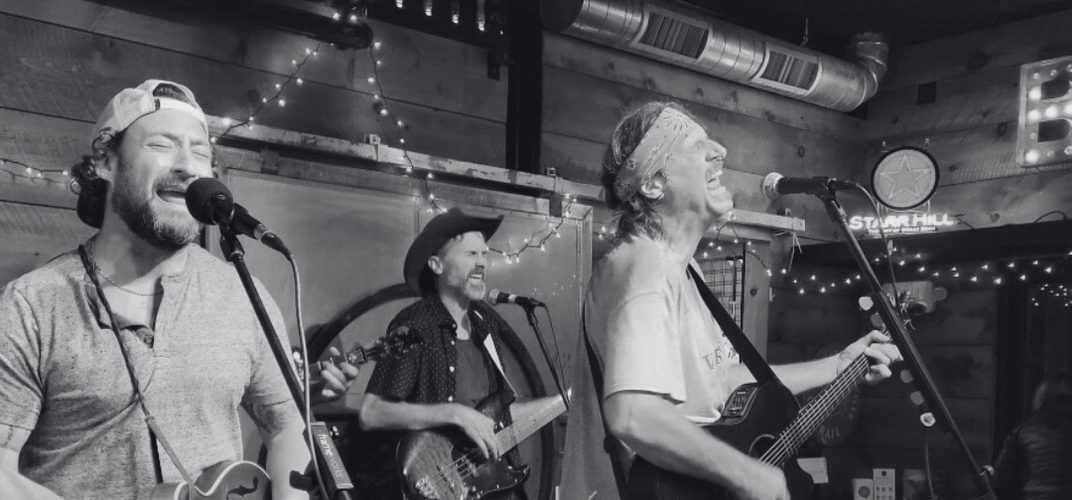 Three members of the South River Strings Band singing into microphones on a small stage