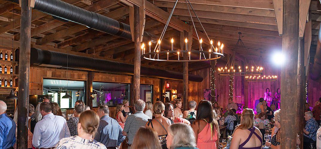A timber-framed tasting barn full of guests under iron chandeliers